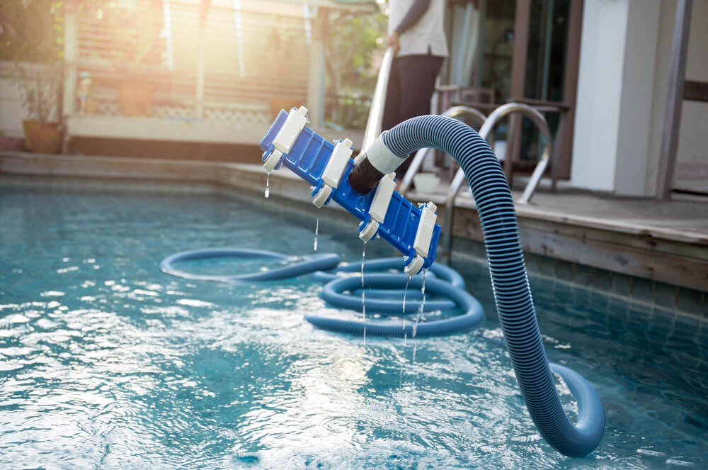 Man Cleaning Swimming Pool With Vacuum Tube Cleaner Early in the Morning