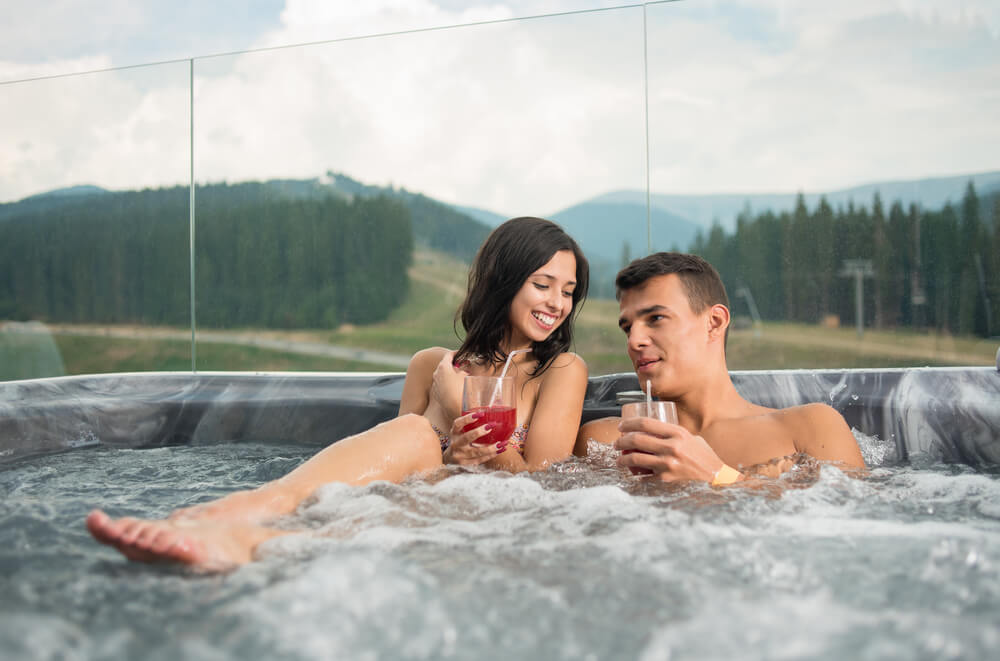 Happy Romantic Couple Enjoying a Bath in Jacuzzi While Drinking Cocktail Outdoors on Romantic Vacation