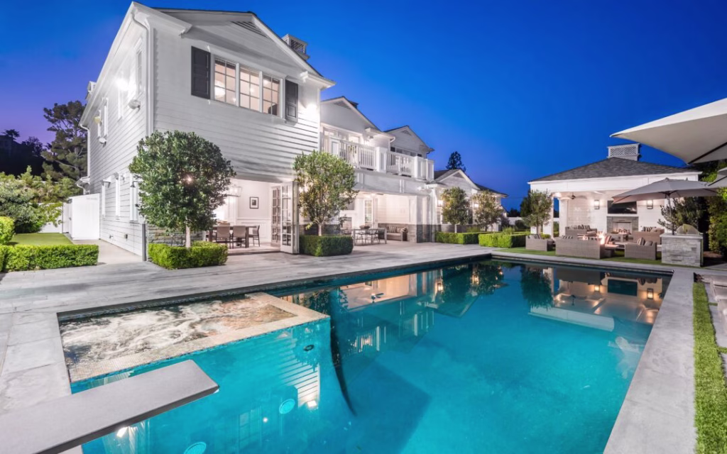 Luxury swimming pool with an attached spa surrounded by sleek stone paving and manicured landscaping at dusk, showcasing a completed pool deck remodel for a modern two-story estate.